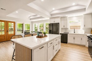 Une cuisine moderne avec des meubles blancs, un grand îlot central et un coin repas baigné de lumière naturelle.
