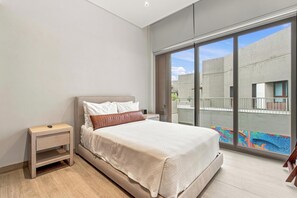 A modern bedroom with a large bed, a nightstand, and a view of a courtyard through a sliding glass door. - Paraíso Residence: Luxury in the Heart of the Marina (Cabo San Lucas)