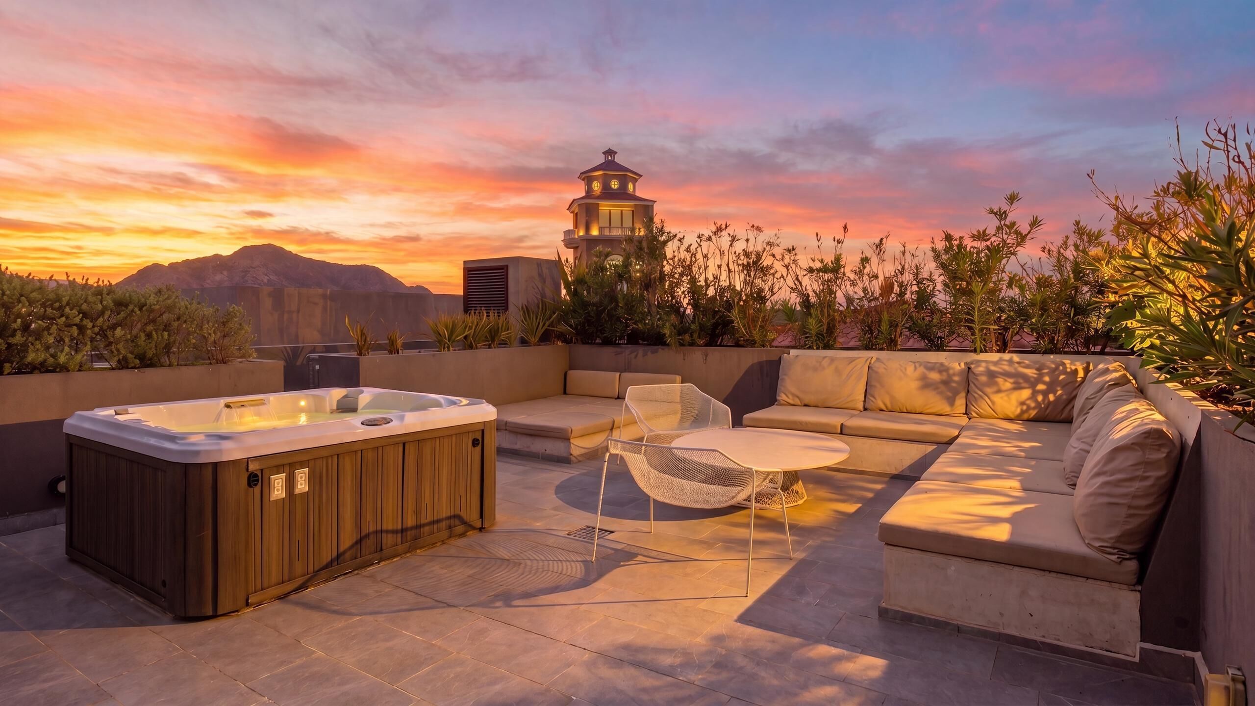 A rooftop terrace with a hot tub, seating area, and a view of a mountain and a lighthouse.