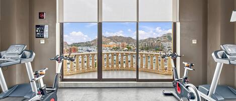 A gym with two treadmills, a large window with a view of a marina and buildings, and a sign indicating no smoking.