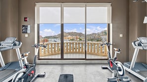 A gym with two treadmills, a large window with a view of a marina and buildings, and a sign indicating no smoking. - Paraíso Residence: Luxury in the Heart of the Marina (Cabo San Lucas)