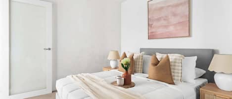 Quarto com cama, mesas de cabeceira, abajur e um quadro na parede.