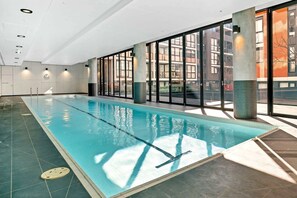 An indoor swimming pool with clear glass walls, a tiled floor, and a view of the outside buildings. - Bright Yarra Side 2BR, Modern Comfort & City Vibes (Abbotsford)