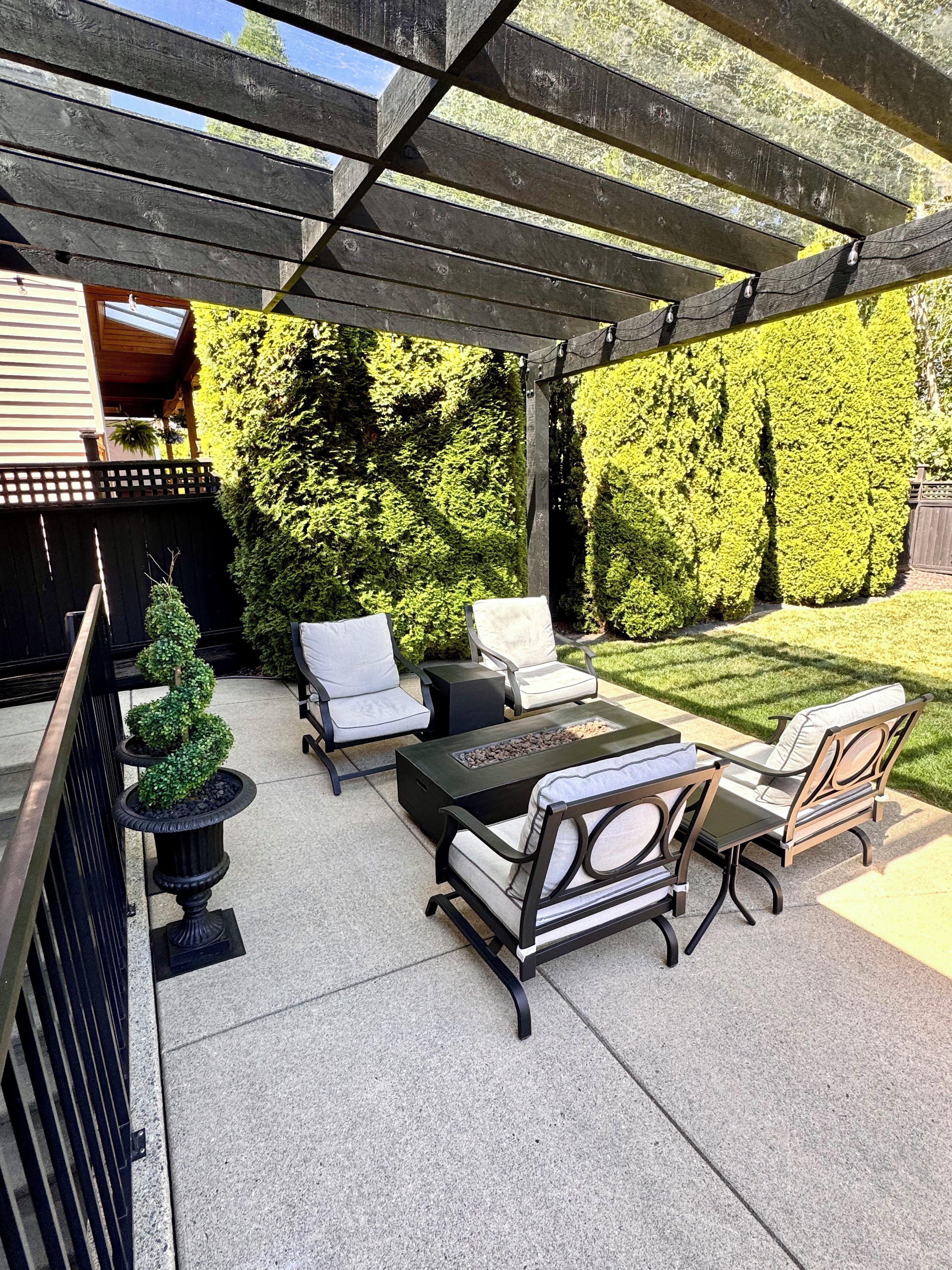 Een terras buiten met een pergola, zithoek en een vuurplaats.