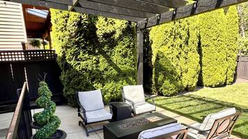 Een terras buiten met een pergola, zithoek en een vuurplaats.