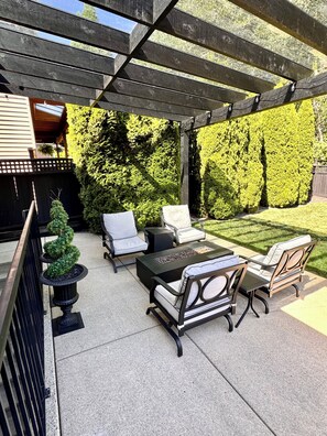 An outdoor patio with a pergola, seating area, and a fire feature.