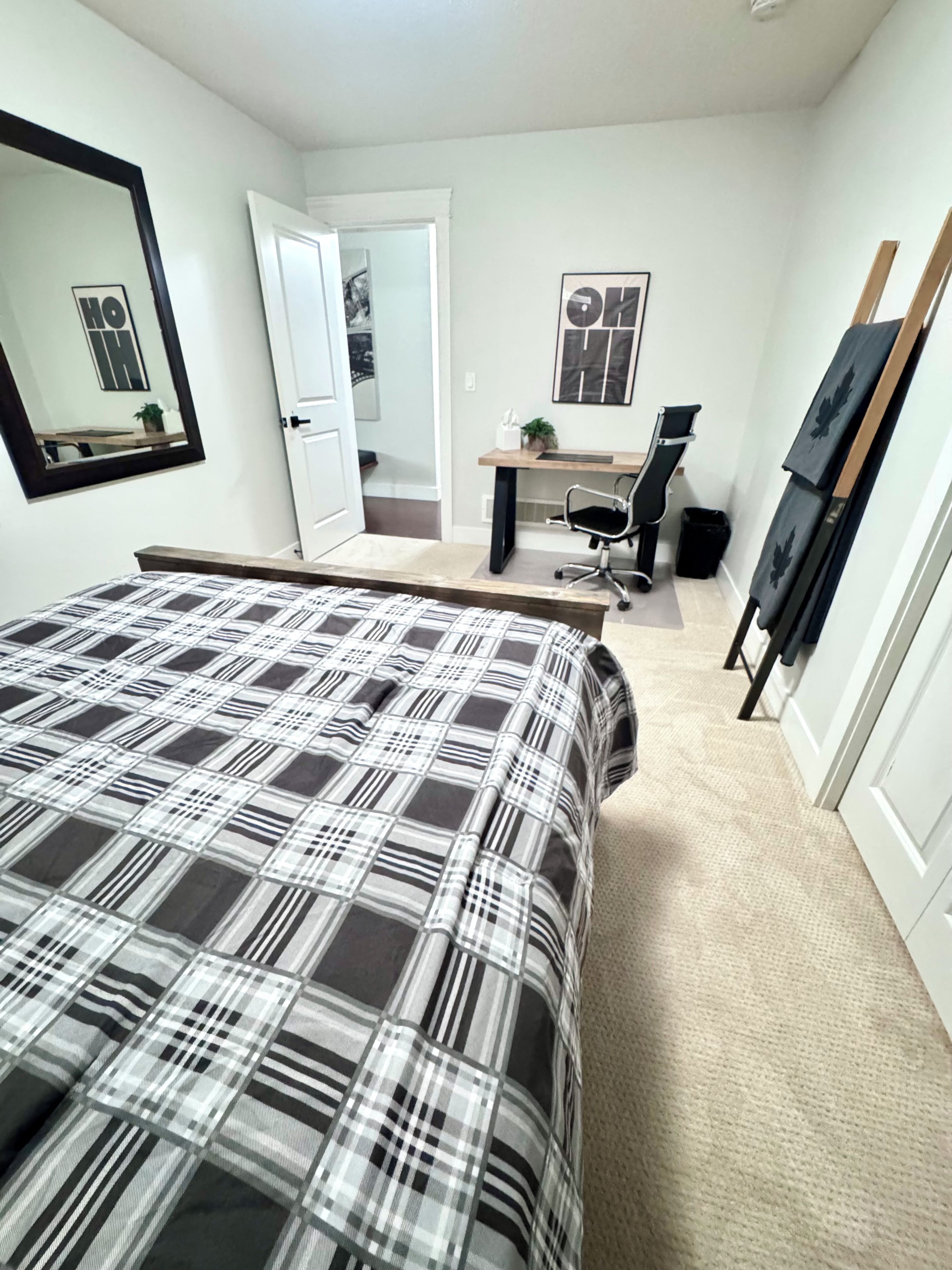 A bedroom with a bed, a desk, a chair, and a door leading to another room.