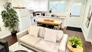 Una sala de estar moderna con un sofá color beige, una mesa de centro y una zona de comedor con una mesa y sillas de madera.