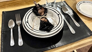 Una mesa lista para comer, con platos, cubiertos, una botella de vino y un frutero.