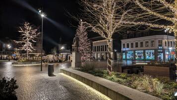 Una plaza urbana nocturna con pavimento de adoquines, árboles iluminados y una estatua.