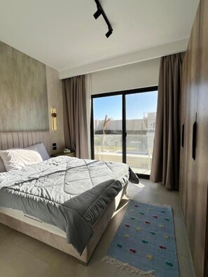 Un dormitorio moderno con una cama grande, una mesita de noche, una ventana con cortinas y vistas al exterior.