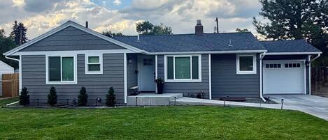 A two-story house with a front garage, a well-maintained lawn, and a large tree to the right.