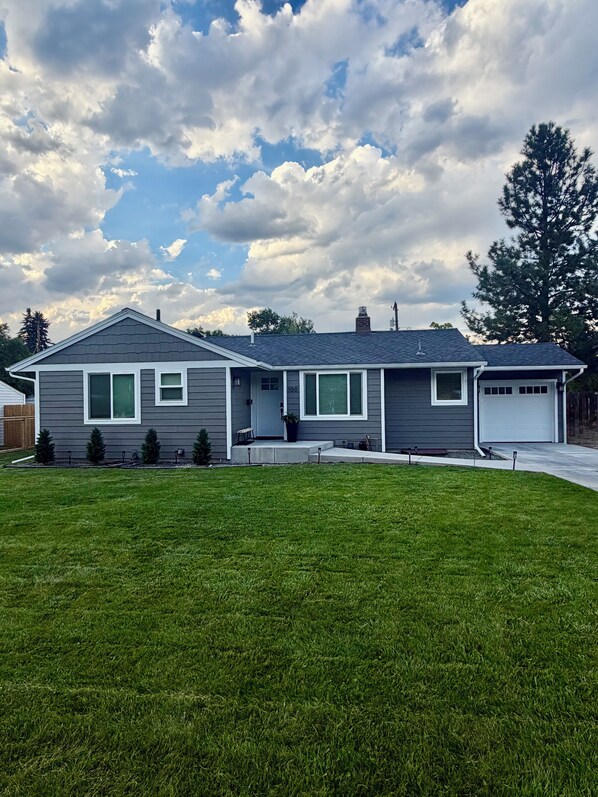 A two-story house with a front garage, a well-maintained lawn, and a large tree to the right.