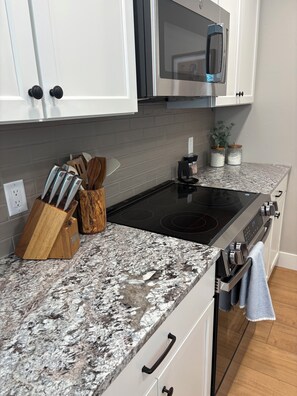 A kitchen with white cabinets, a granite countertop, a black induction cooktop, and a stainless steel oven. - Spacious 4-bedroom, 5 bed, Family House with AC in perfect Missoula location (Missoula)
