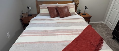 Une chambre à coucher avec un lit, une table de chevet, une lampe, une fenêtre et un tableau accroché au mur.