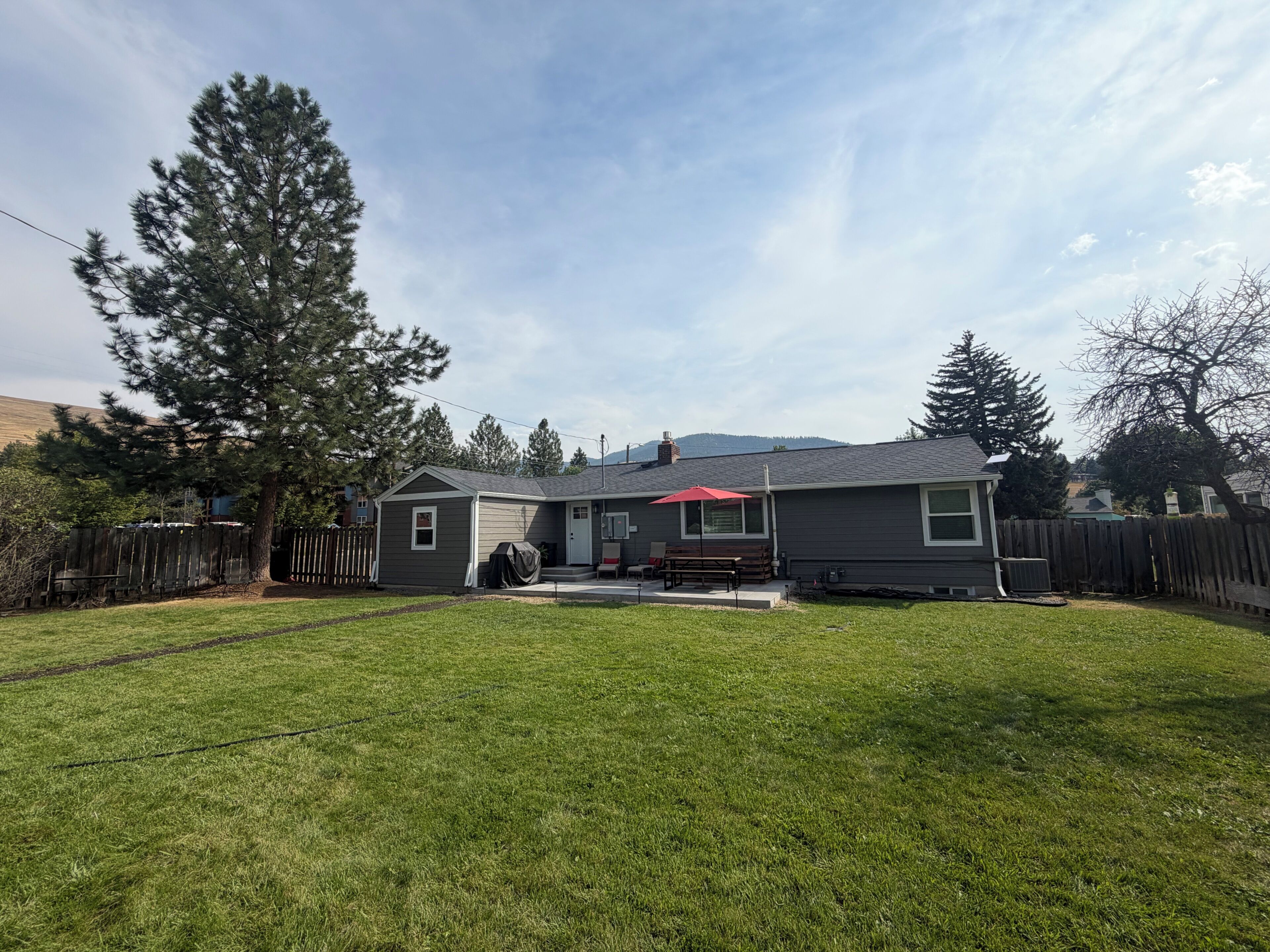 A residential property with a well-maintained lawn, a wooden deck, and a house with a red umbrella.