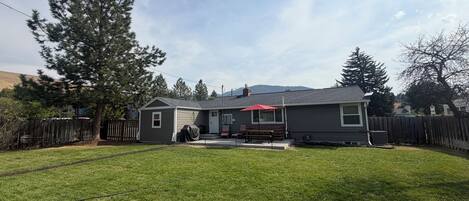 A residential property with a well-maintained lawn, a wooden deck, and a house with a red umbrella.