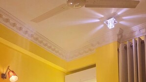 A hotel room with a large bed, a ceiling fan, a window with curtains, and a wall-mounted air conditioning unit. - Luxury 3BR Apartment Nugegoda bordering Colombo 5 (Nugegoda)