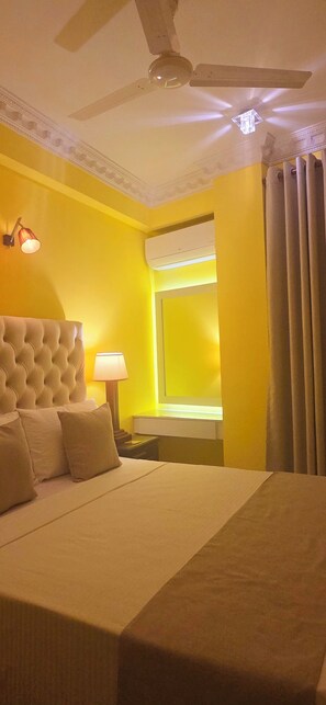 Ein Hotelzimmer mit einem großen Bett, einem Deckenventilator, einem Fenster mit Vorhängen und einer Wand-Klimaanlage.