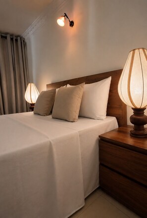 Ein Hotelzimmer mit einem aufgeräumten Bett, zwei Nachttischlampen, einem Holznachttisch und einer Wandleuchte.