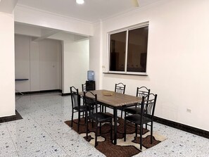 A dining area with a table and chairs, a water dispenser, and a window with blinds. - Modern 3BR Nyali Apartment with AC, Wi-Fi and Backup Generator (Mombasa)