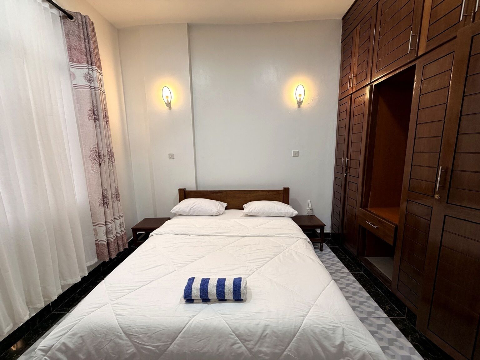 Une chambre à coucher avec un lit, deux tables de chevet, une armoire et un rideau.