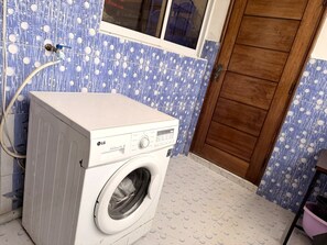 Una lavadora blanca en una habitación con baldosas azules con lunares y una puerta de madera.