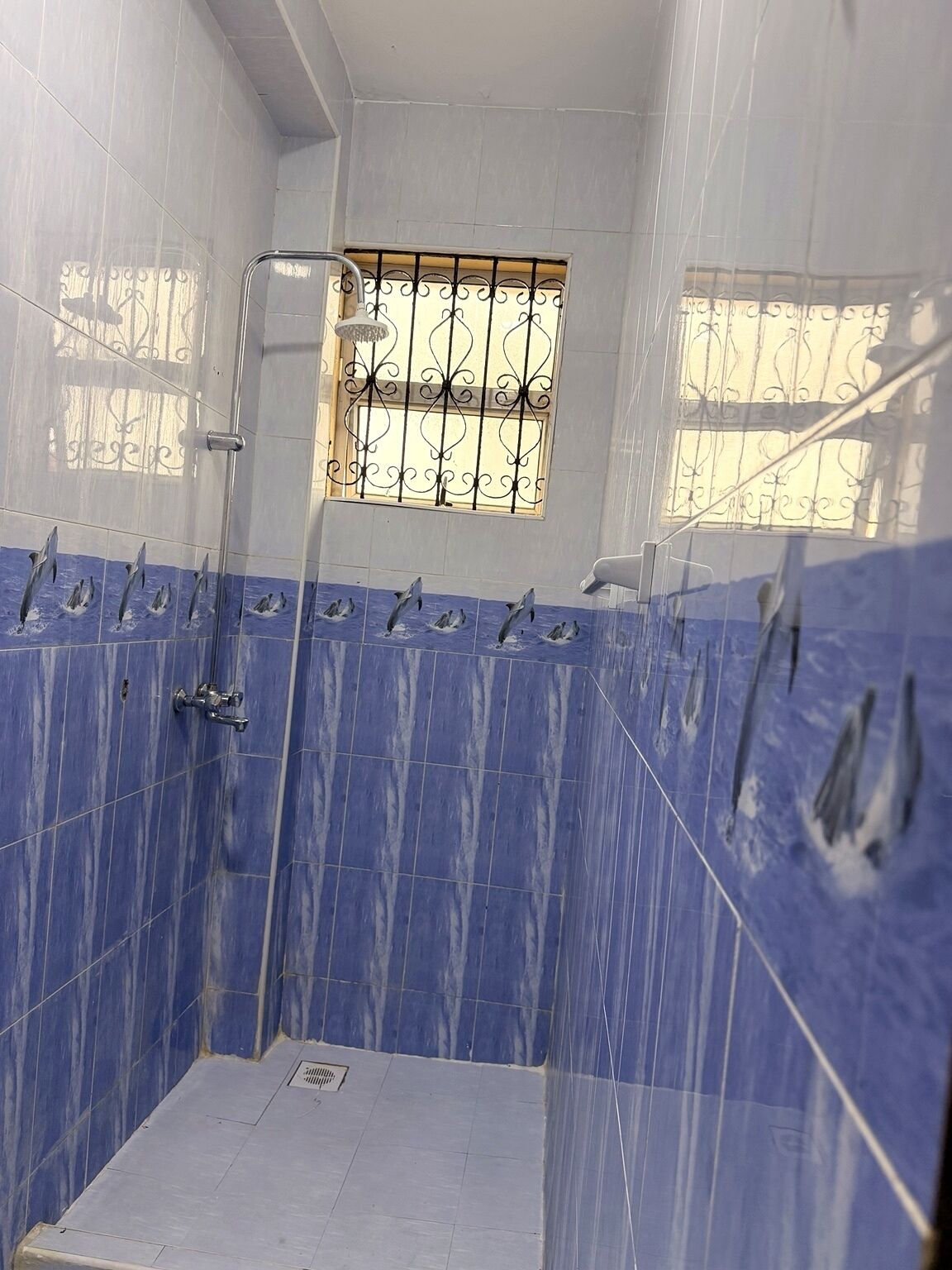 A bathroom with blue-tiled walls, a shower area, and a window with decorative iron bars.