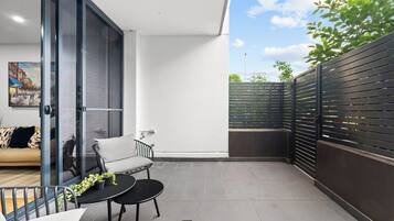 A modern balcony with a sofa, a small table with plants, and a view of the sky and greenery.