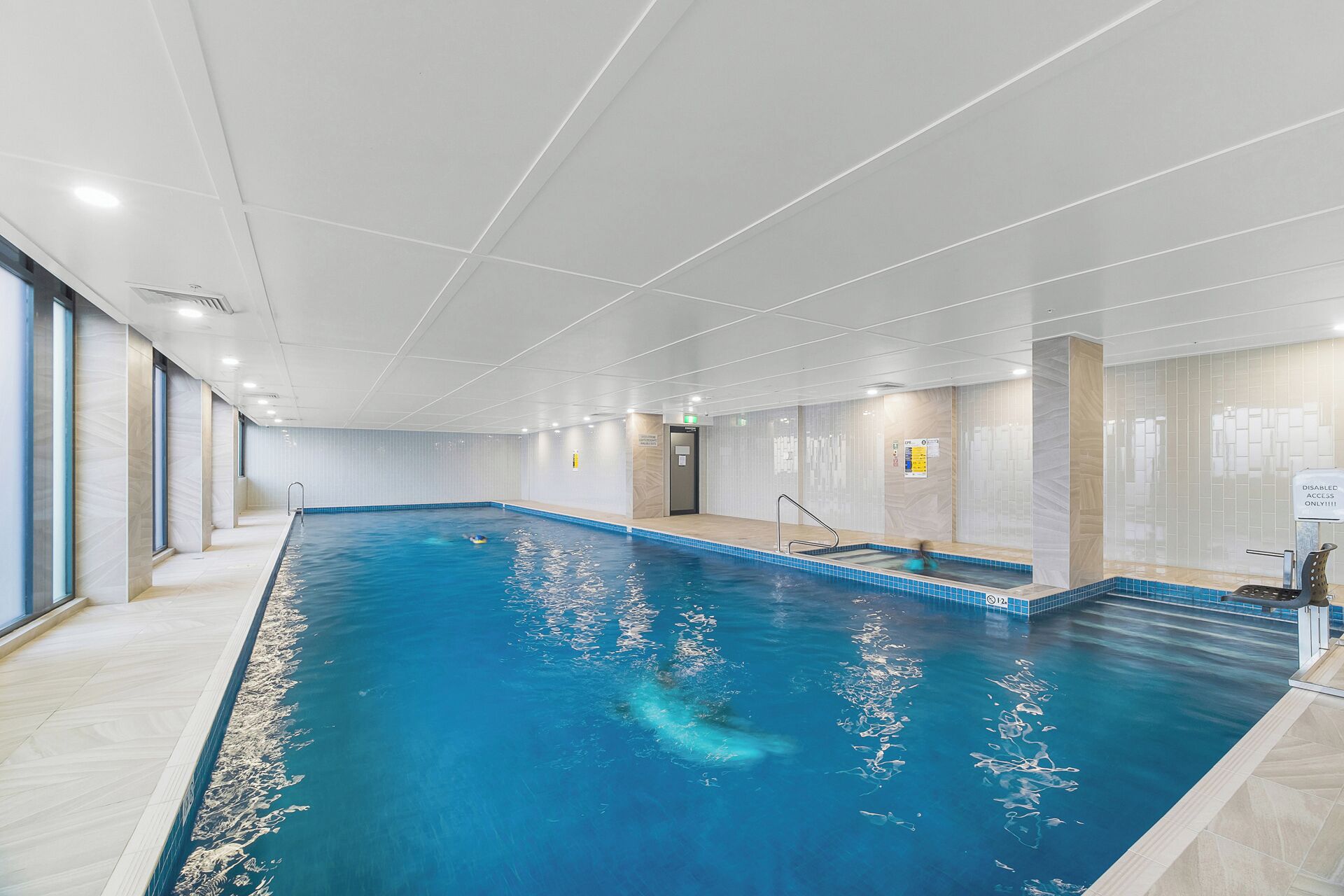 An indoor swimming pool with clear water, tiled walls, and a tiled floor.