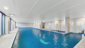 An indoor swimming pool with clear water, tiled walls, and a tiled floor.