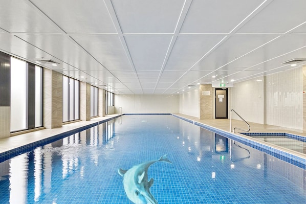 An indoor swimming pool with clear blue water, a dolphin decoration, and a door on the right side.