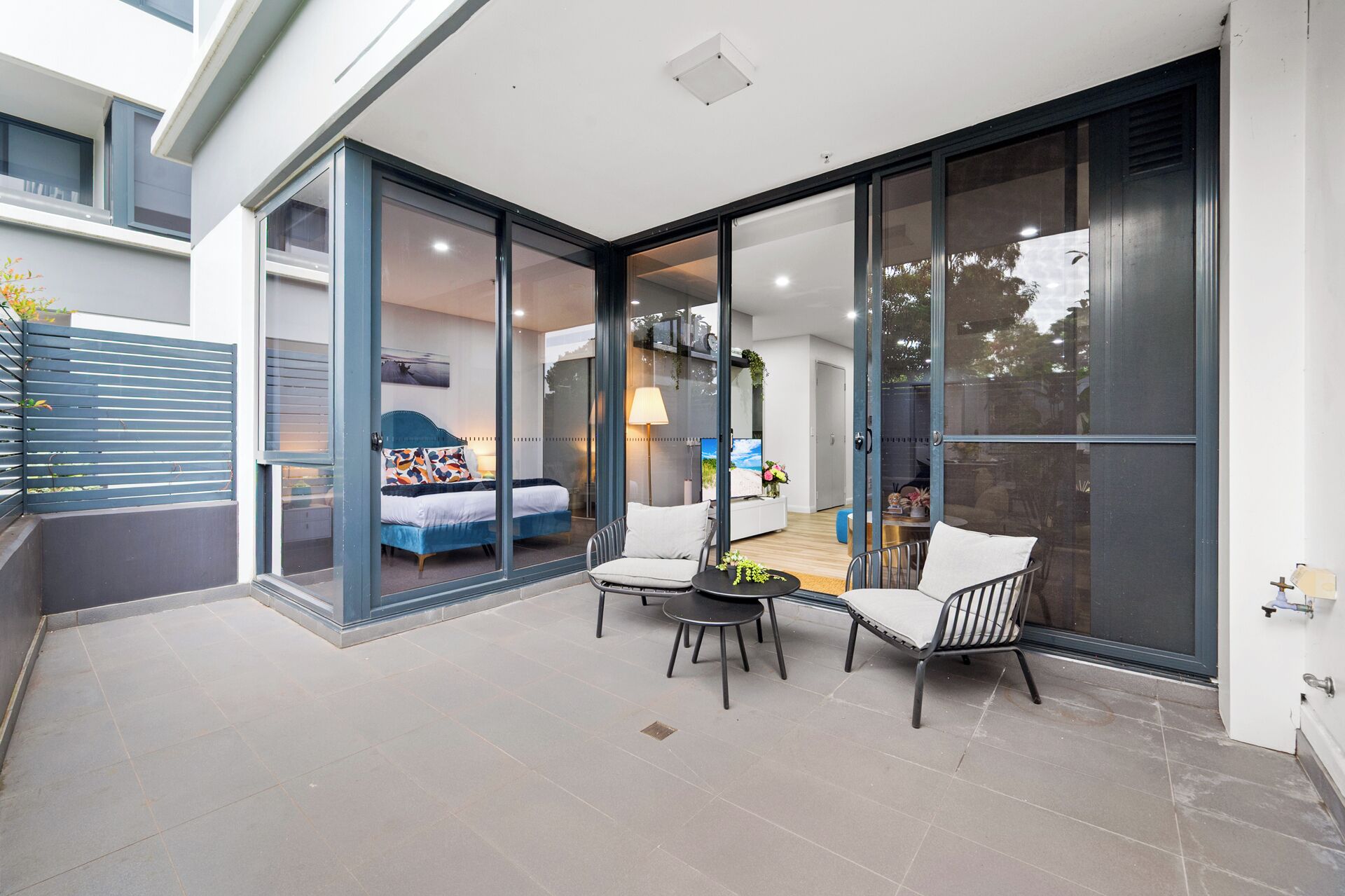 A modern patio with a bed, two chairs, and a table.
