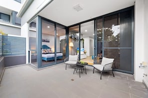 A modern patio with a bed, two chairs, and a table. - Robbie Williams Stay | Walk to Accor Stadium | Sydney Olympic Park (Sydney Olympic Park)