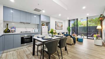 A modern kitchen with grey cabinets, a dining area with a table set for two, and a view of a garden through large sliding doors.