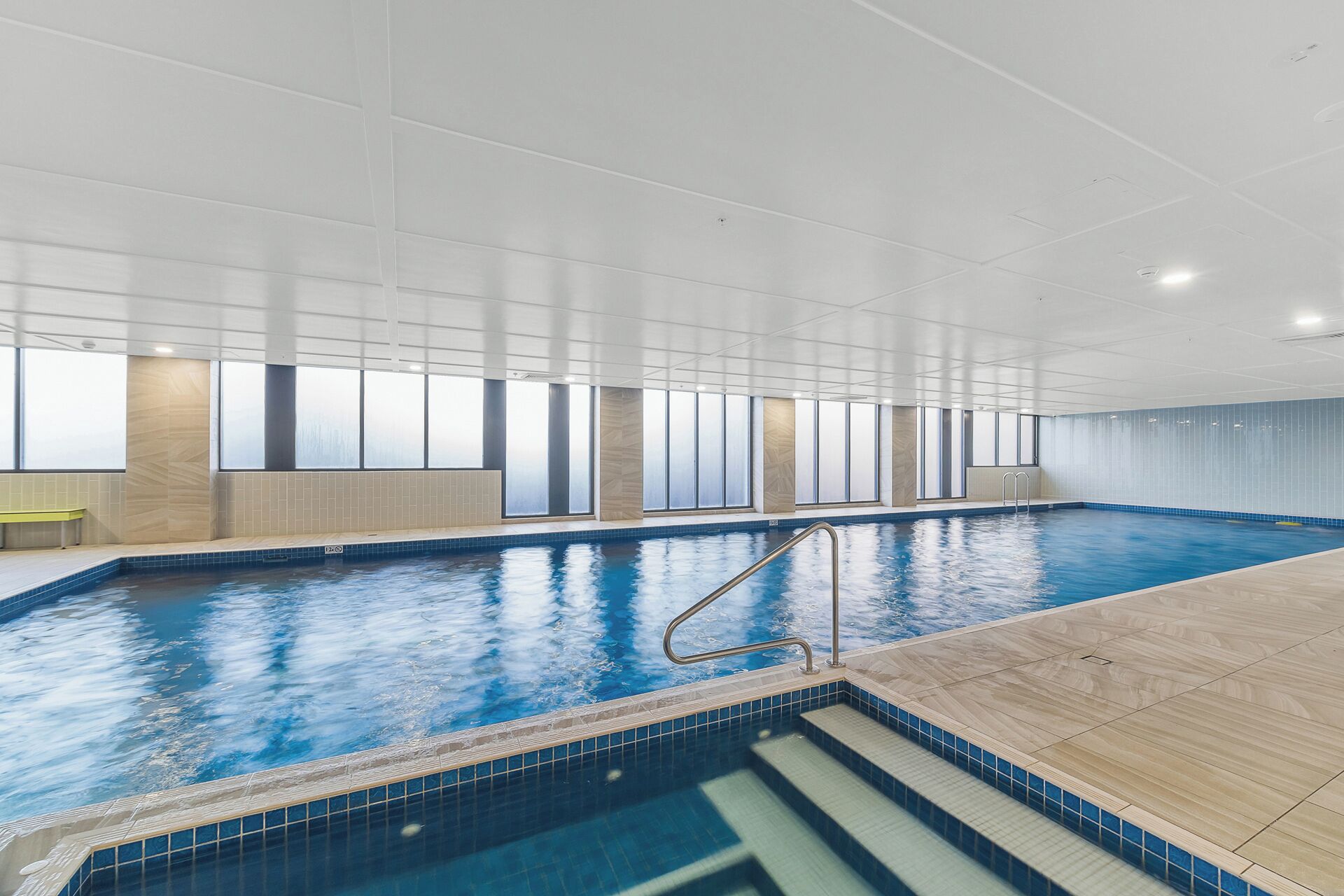 An indoor swimming pool with clear water, a wooden deck, and a metal ladder.