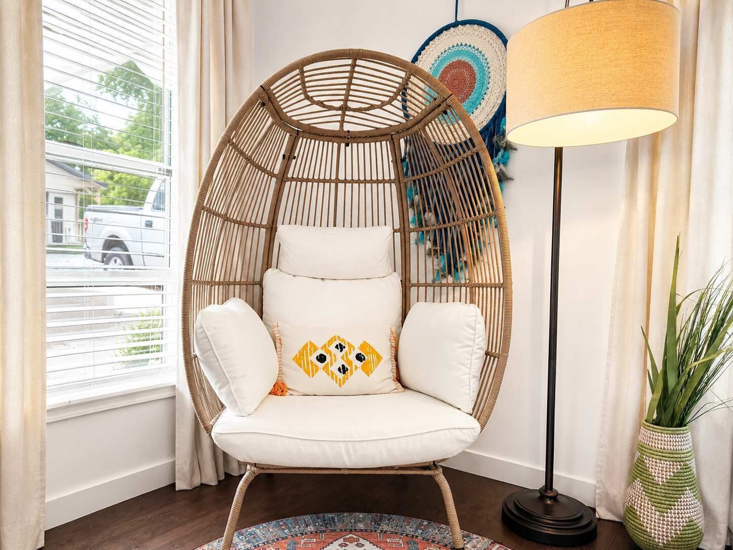 A room with a rattan chair, a floor lamp, a wall hanging, and a potted plant.