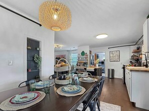 A dining area with a wooden table set for four, a hanging light fixture, and a kitchen in the background. - Boho Bungalow, pet friendly house walk to downtown (Branson)