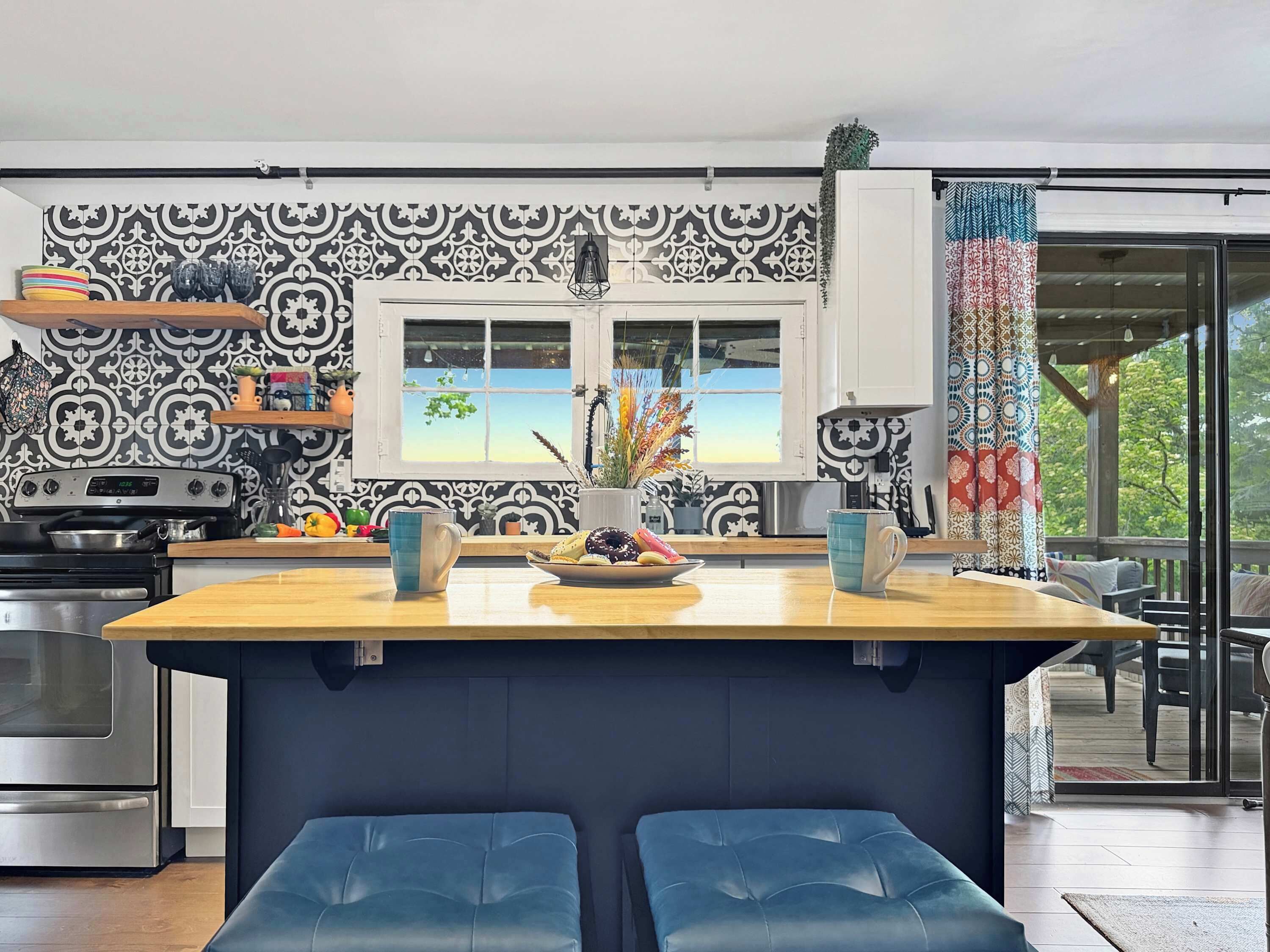 Une cuisine moderne avec un îlot central, un coin repas avec des chaises bleues et une vue par la fenêtre.