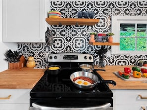 A kitchen with a stove, pots, and a variety of utensils. There is a window with a view of greenery. - Boho Bungalow, pet friendly house walk to downtown (Branson)