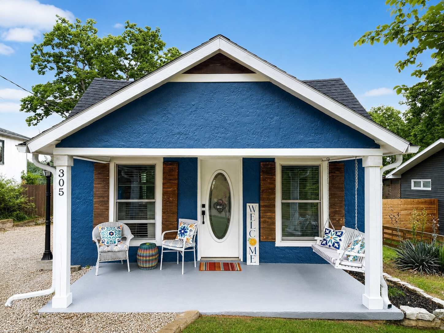 Une maison à l’extérieur bleu, avec un porche blanc et une enseigne accueillante.