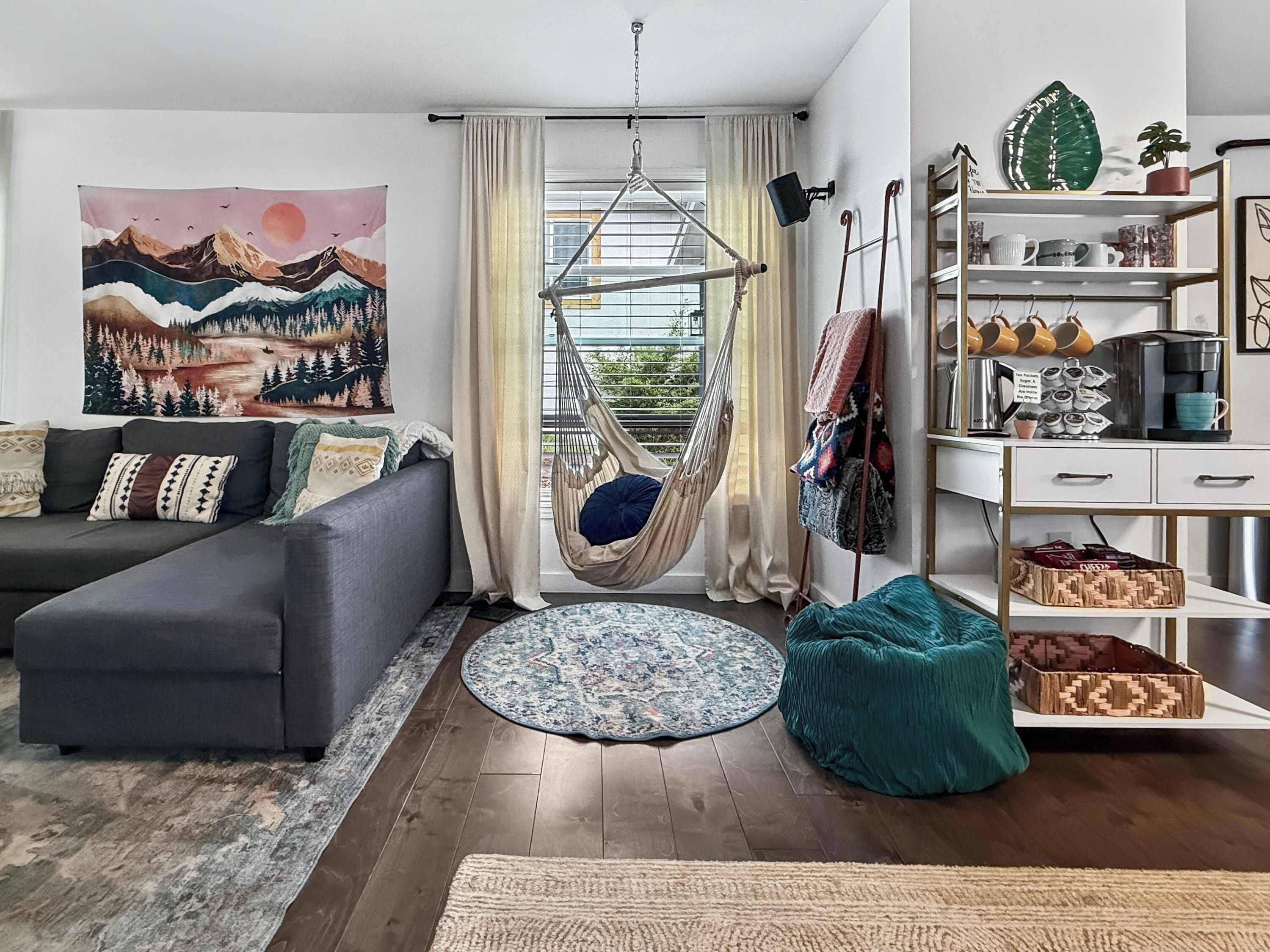 Un salon moderne avec un canapé, un fauteuil suspendu, un tapis rond et une bibliothèque.