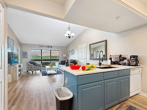 Une cuisine moderne dotée d’un grand îlot central, d’un coin repas offrant une vue agréable et d’un salon avec un canapé et une table basse.