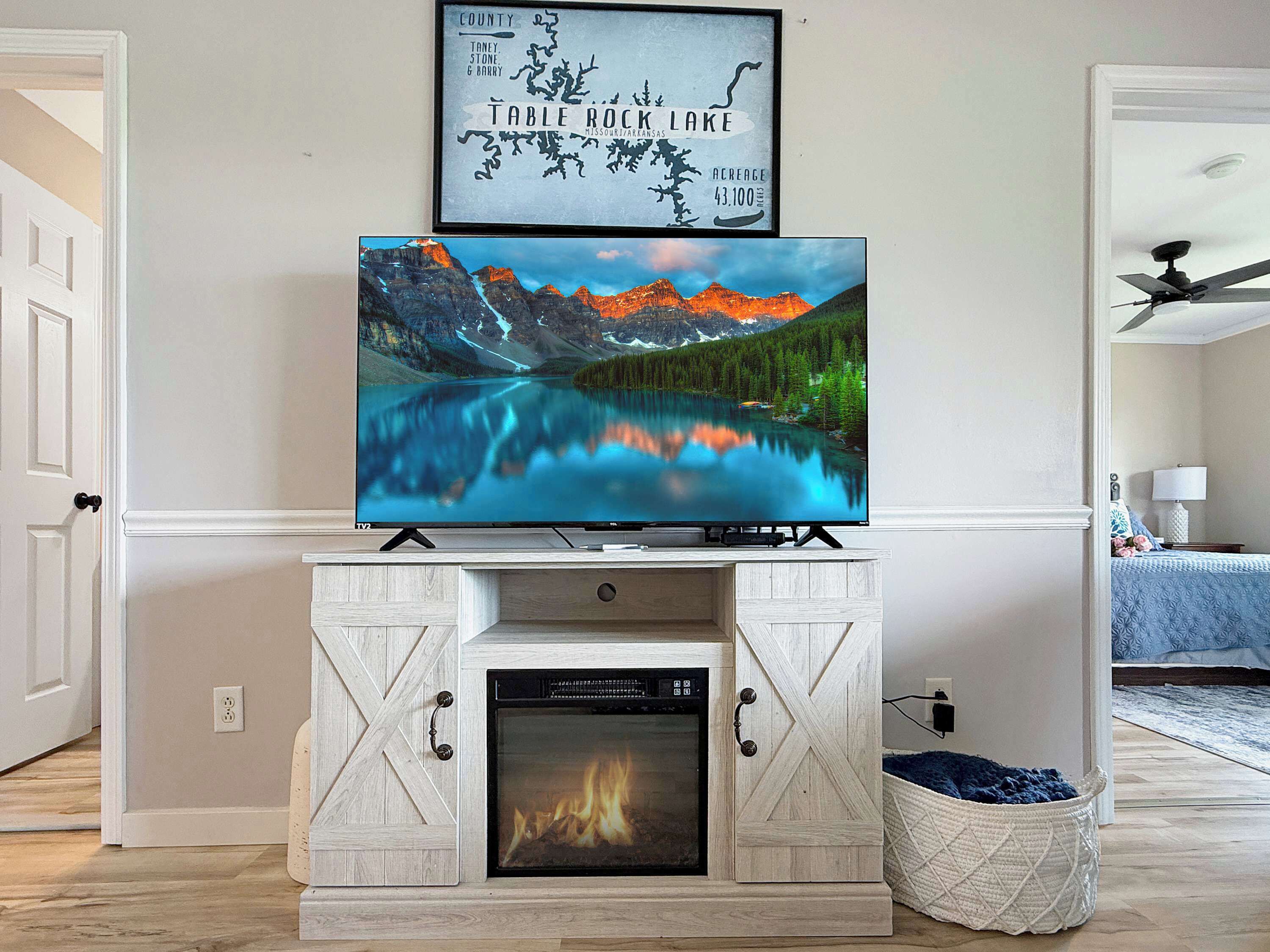 A TV mounted on a wooden cabinet above a fireplace with a framed picture of a lake.