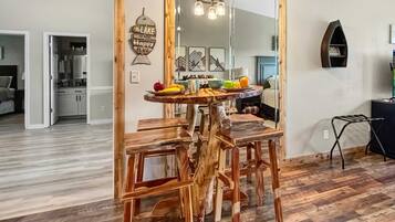 A dining area with a wooden table and chairs, a mirror reflecting the room, and a sign on the wall.