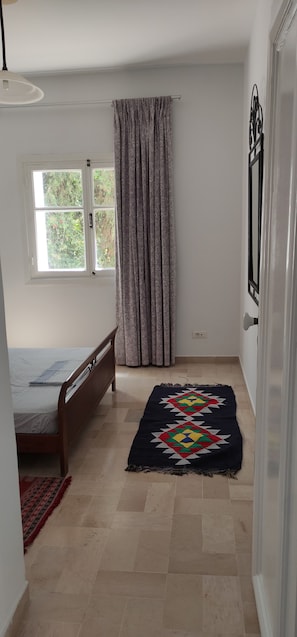 Une chambre à coucher avec un lit, une fenêtre avec des rideaux, une porte et un tapis à motifs.