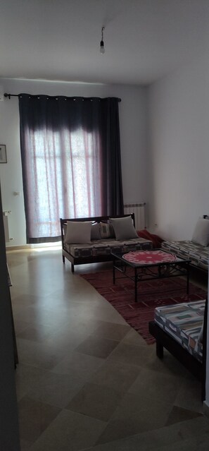 Una habitación con cama, sofá, una mesita de centro y una ventana con cortinas.
