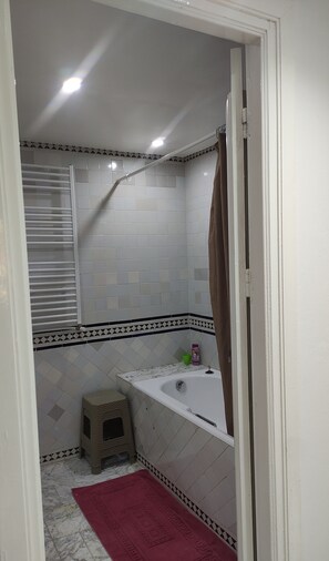 Ein Badezimmer mit weißen Fliesen, einer Duschkabine, einer Badewanne und einem kleinen Hocker.