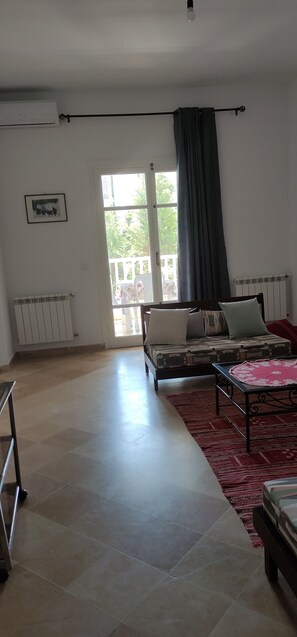 Ein Wohnzimmer mit einer Couch, einem Couchtisch, einer Heizung und einem großen Fenster mit Vorhängen.