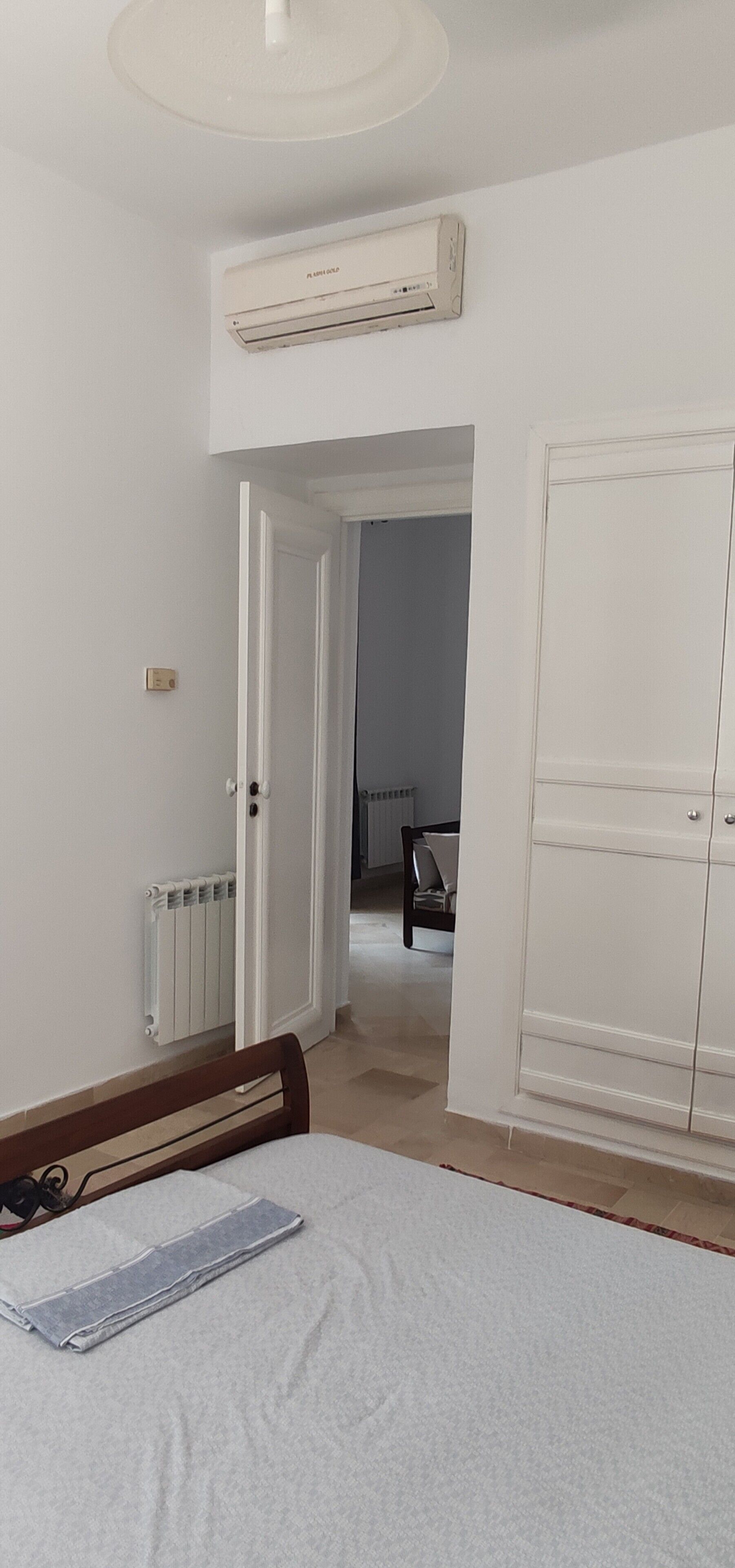 A bedroom with a bed, a radiator, a wardrobe, and an air conditioning unit.